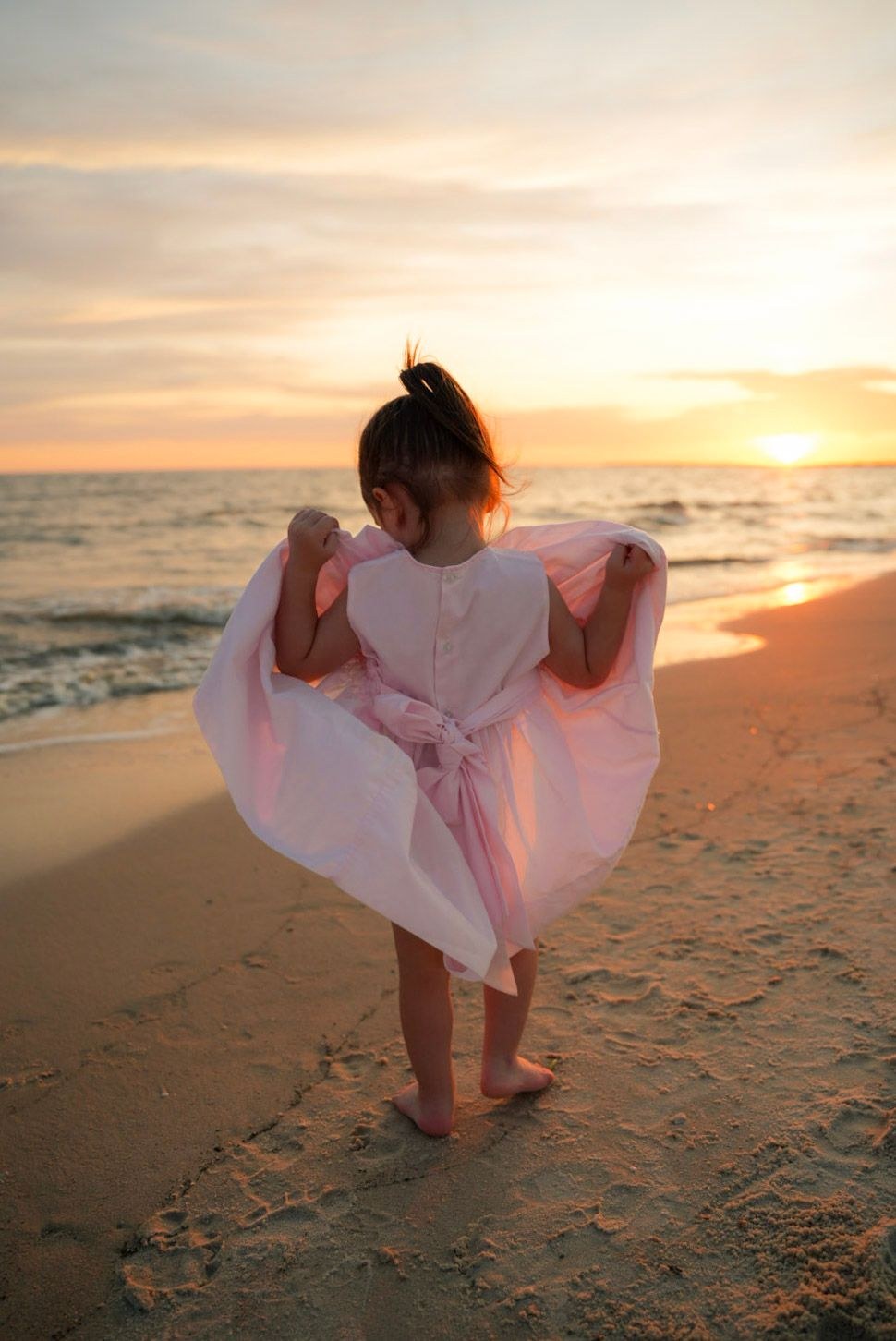 Little girl in a pink dress twirling on the beach at sunset